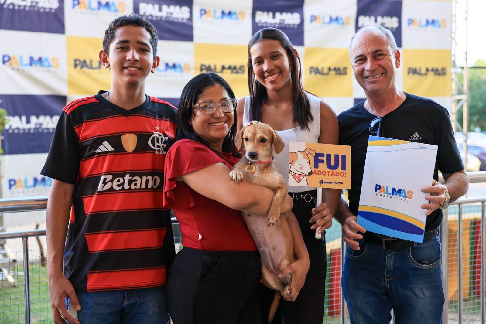 Grupo posa com cachorro caramelo e placa com a frase Fui adotado em ação de proteção animal.
