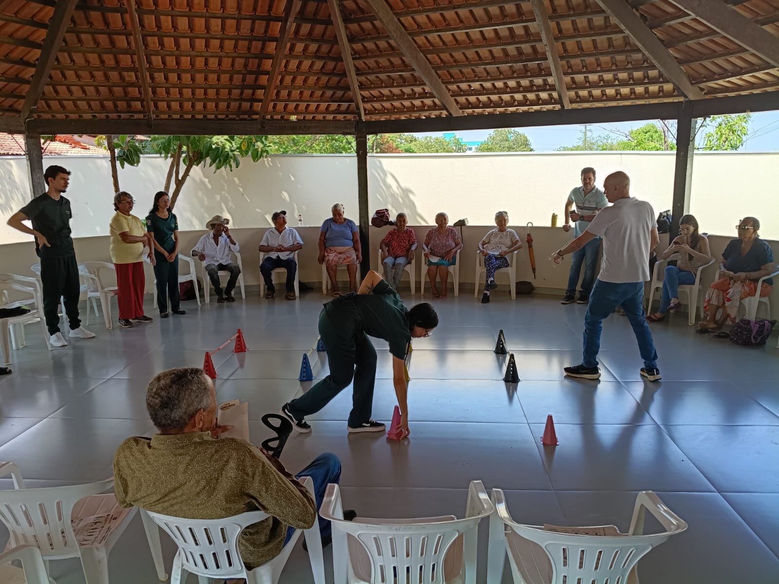 Pessoas idosas acompanham atividade com cones e pequenas barreiras em espaço coberto.