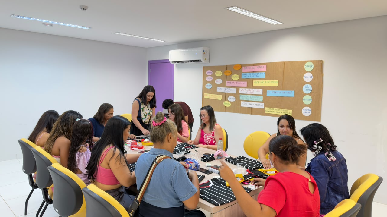 Participantes customizam peças listradas com fitas e materiais de artesanato ao redor de uma mesa.
